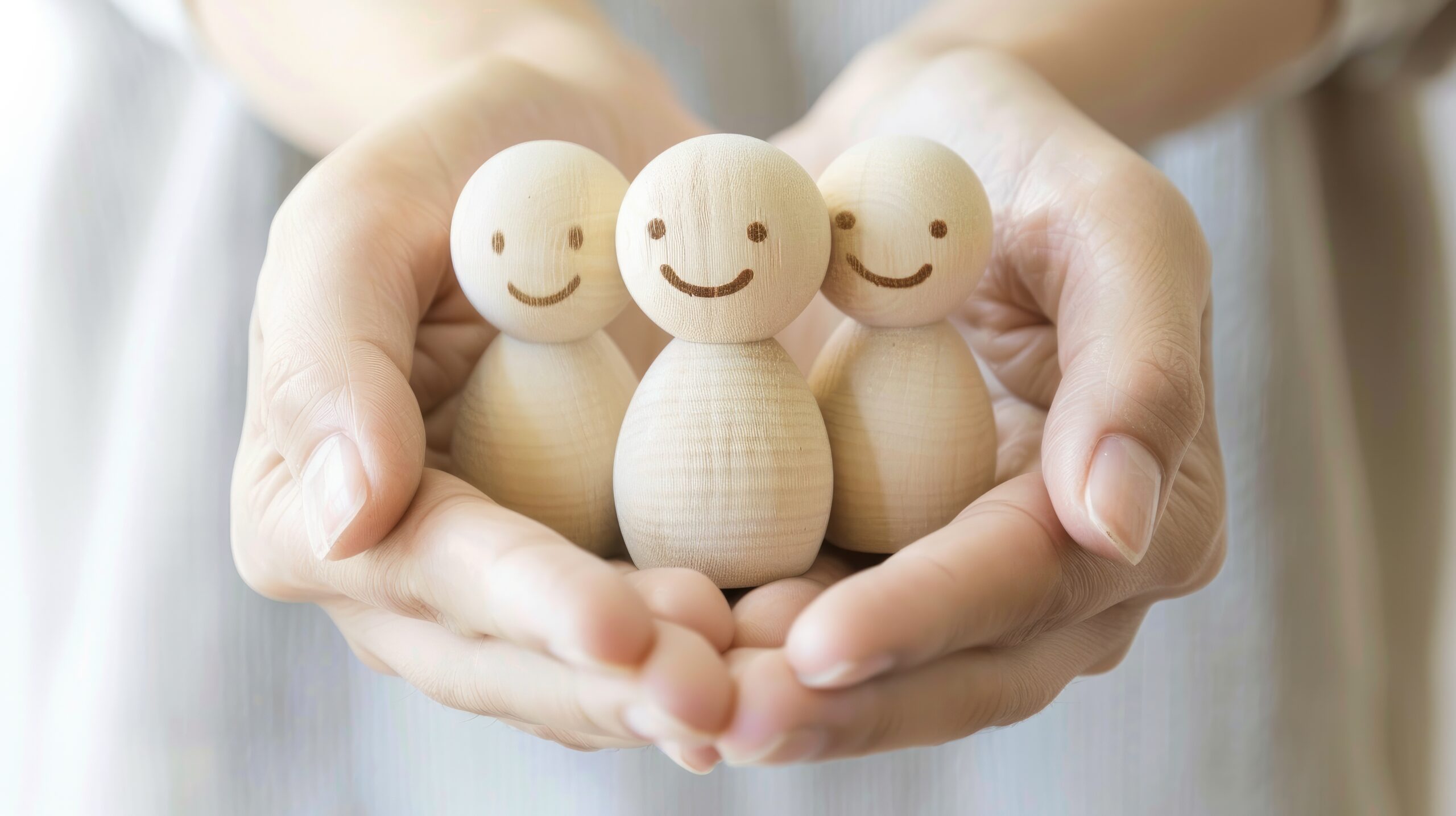 Hands Holding Wooden Figures Representing Family Protection and Care through Life Insurance and Health Cover